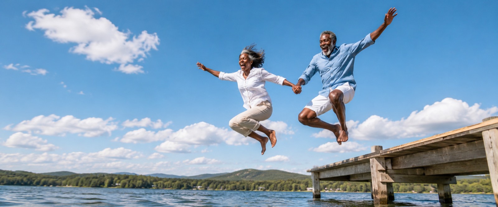 A couple in their sixties leaping hand in hand off a wooden jetty into a lake.